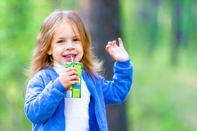 Fröhliches kleines Mädchen trinkt Saft im Freien Spaziergang im Wald Sommer sonniger Tag