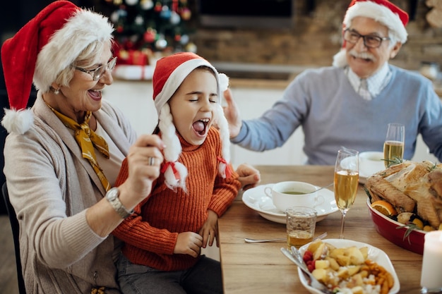 Fröhliches kleines Mädchen und ihre Großeltern amüsieren sich beim Weihnachtsessen zu Hause