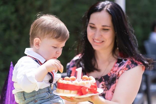 Fröhliches Kleinkind und seine Mutter freuen sich über seinen Geburtstag und essen einen Kuchen mit einer Kerze