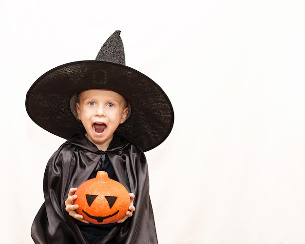 Fröhliches lachendes Kind mit einem Kürbis in schwarzem Hut und Umhang Das Konzept des Feiertags Halloween