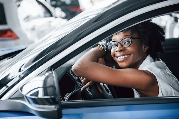 Fröhliches Lächeln. Junge Afroamerikanerin sitzt im neuen modernen Auto.