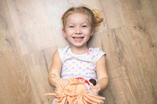 Fröhliches lächelndes Kindermädchen, das ein Spielzeug hält, das auf einem Holzboden liegtDraufsicht liegt flach