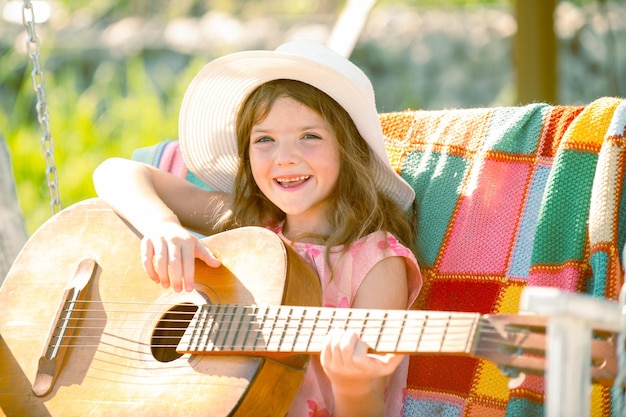 Fröhliches lächelndes Kindermädchen spielt Gitarre Kindermusik und Lieder lächelndes Kind, das im Sommer im Freien spielt