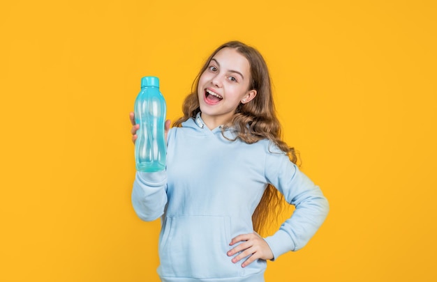 Fröhliches lächelndes Mädchen hält eine Wasserflasche zum Trinken nach dem Sporttraining durstig