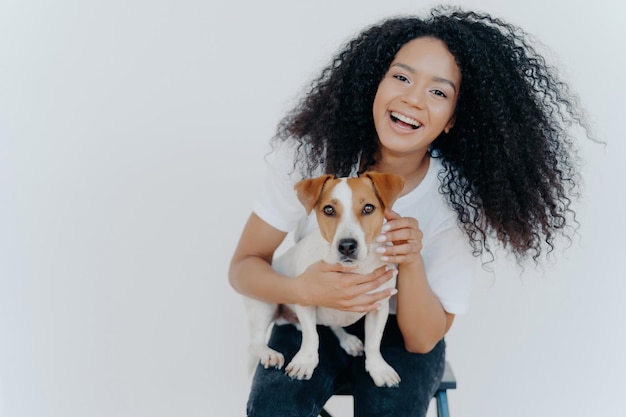 Fröhliches, lockiges Mädchen mit neuem Jack Russell Terrier, lächelnd, spielend und streichelnd. Glückliche Momente, festgehalten in einem isolierten Porträt