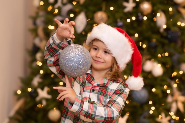 Fröhliches lustiges Kind mit Weihnachtsmütze in der Nähe von Weihnachtsbaum Weihnachten und Winterurlaub Konzept des neuen Jahres