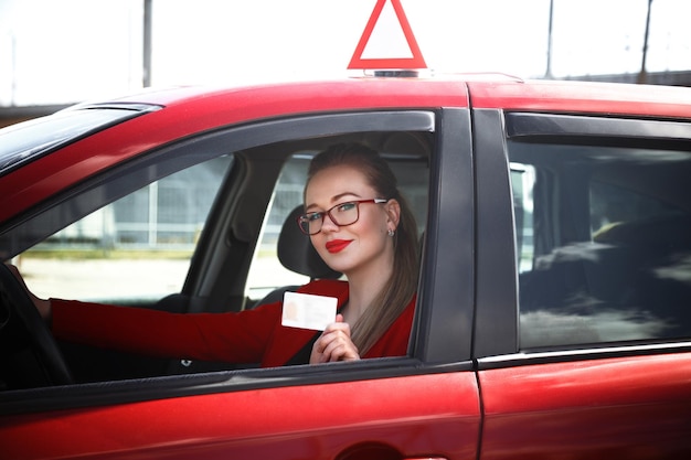 Fröhliches Mädchen, das ein Trainingsauto mit einem Führerschein in den Händen fährt.