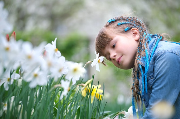 Fröhliches Mädchen, das im Sommergarten den süßen Duft weißer Narzissenblüten genießt