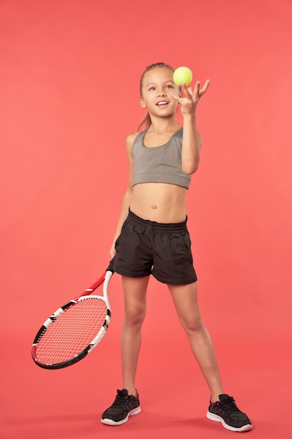 Fröhliches Mädchen, das Schläger hält und mit Tennisball spielt