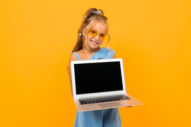 Fröhliches Mädchen im Kleid lächelt mit ihrem Laptop lokalisiert auf Gelb und Orange