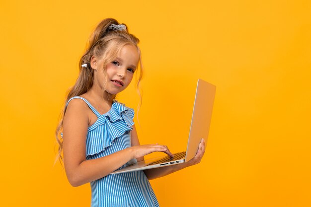 Fröhliches Mädchen im Kleid lächelt mit ihrem Laptop lokalisiert auf Gelb und Orange