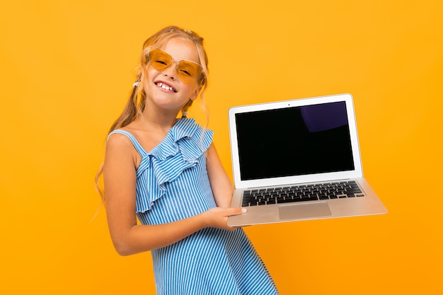 Fröhliches Mädchen im Kleid lächelt mit ihrem Laptop lokalisiert auf gelbem und orange Hintergrund