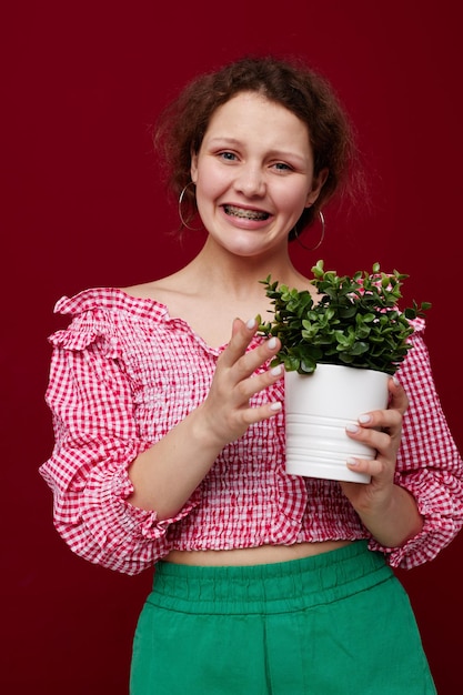 Fröhliches Mädchen in einem rosa Blusentopf mit einer Blume in ihrem roten Hintergrund der Hände