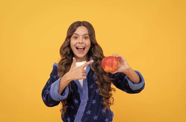Fröhliches Mädchen in Nachtwäsche, das mit dem Finger auf natürliches Essen frischer Apfelfrüchte zeigt