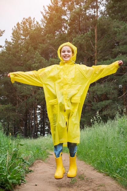 Foto fröhliches mädchen in regenkleidung springt durch grünen wald auf den weg