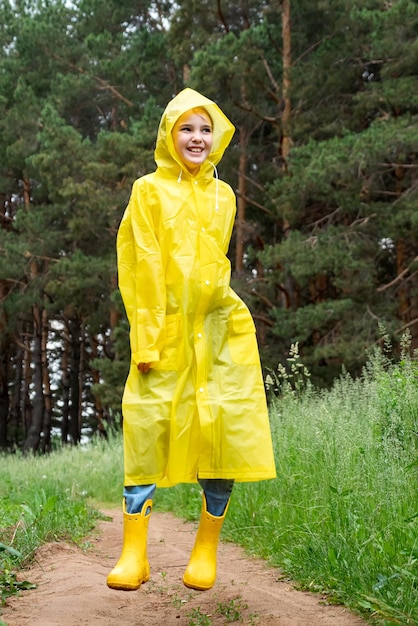 Fröhliches Mädchen in Regenkleidung springt durch grünen Wald auf den Weg