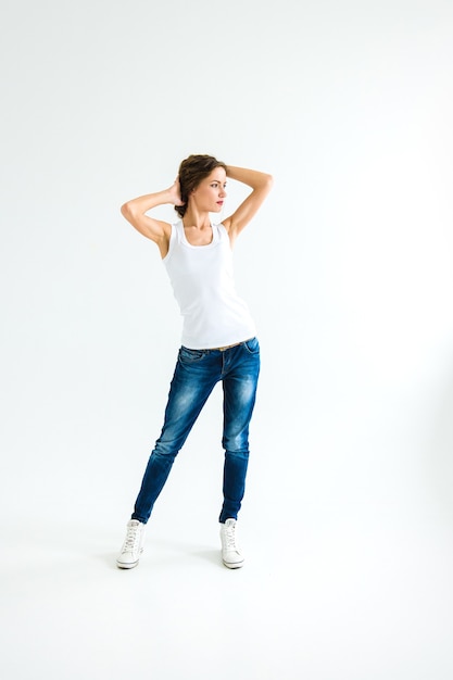 Fröhliches Mädchen in weißem T-Shirt und dunkelblauer Jeans im Studio auf weißem Hintergrund steht, sitzt, läuft