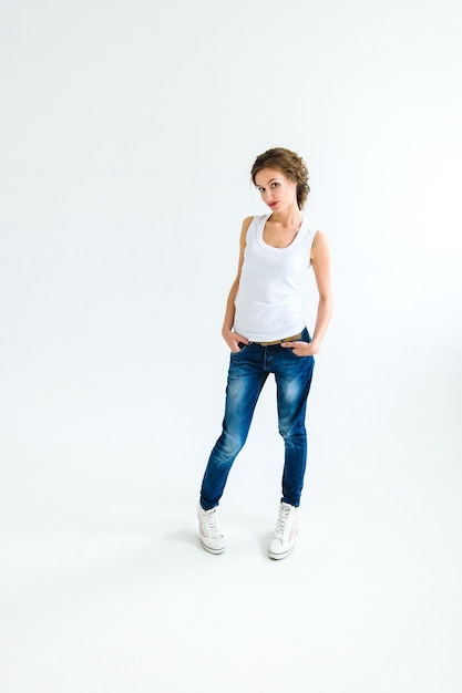 Foto fröhliches mädchen in weißem t-shirt und dunkelblauer jeans im studio auf weißem hintergrund steht, sitzt, läuft