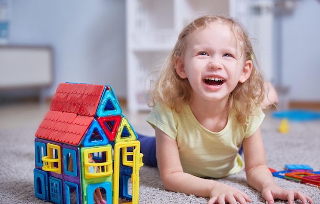 Foto fröhliches mädchen lacht auf dem teppich neben dem spielzeughaus