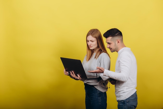 Fröhliches Mädchen mit Freund, das Laptop auf gelbem Hintergrund anschaut Sie studieren zusammen Probleme lösen Lernarbeitskonzept