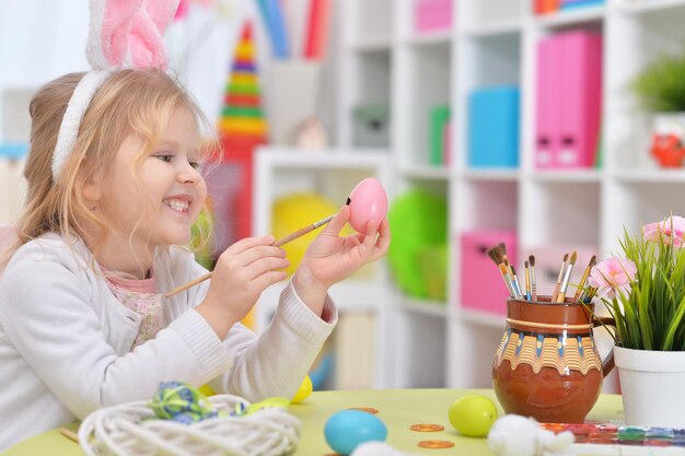 Fröhliches Mädchen mit Hasenohren, das sich auf Ostern vorbereitet und Eier färbt.