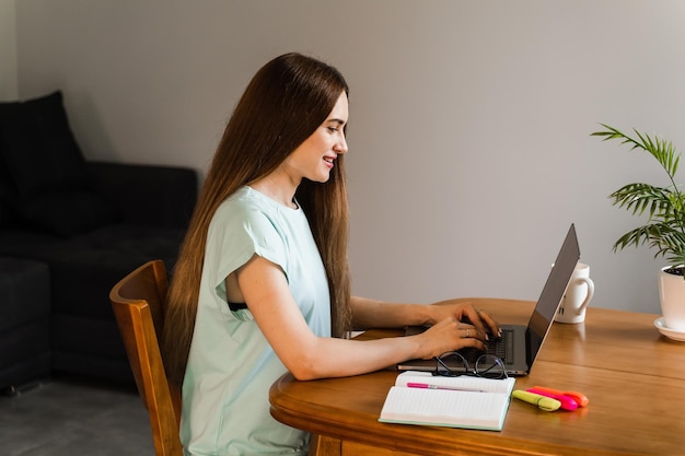 Fröhliches Mädchen mit Laptop, das Text tippt und mit Freunden und Familie zu Hause chattet Junge Frau macht eine Pause, um sich Online-Videos und Schulungen auf dem Laptop anzuschauen, die sich auf die Konferenz vorbereiten