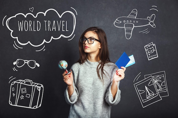 Fröhliches Mädchen mit Pass-Flugticket und Globus vor grauem Hintergrund Indoor-Reisekonzept