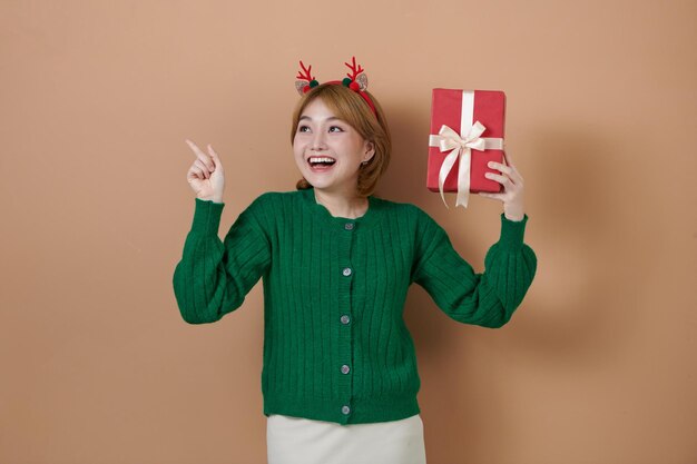 Fröhliches Mädchen mit weihnachtlichen Hirschhörnern, das eine Geschenkbox hält, die auf einen leeren Kopierraum zeigt