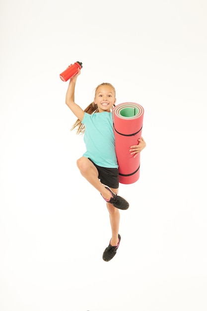 Fröhliches Mädchen mit Yogamatte und Wasserflasche im Studio springen