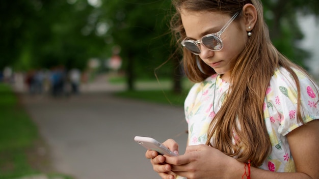 Fröhliches Mädchen spielt im Park am Telefon. Verspieltes Mädchen nutzt Smartphone