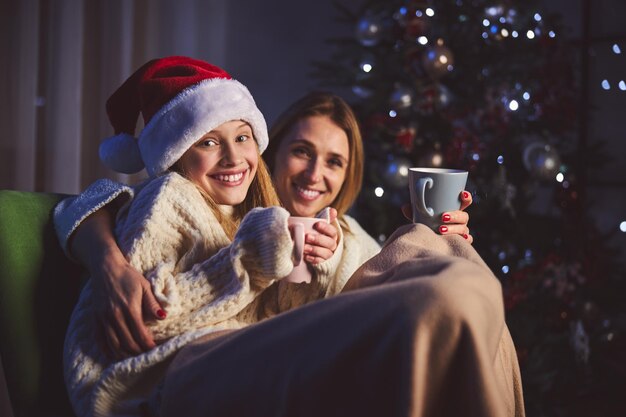 Fröhliches Mädchen und ihre Mutter sitzen am Weihnachtsbaum zu Hause