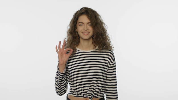 Foto fröhliches mädchen zeigt im studio ein „ok“-zeichen. porträt einer jungen frau, die eine „ok“-geste zeigt