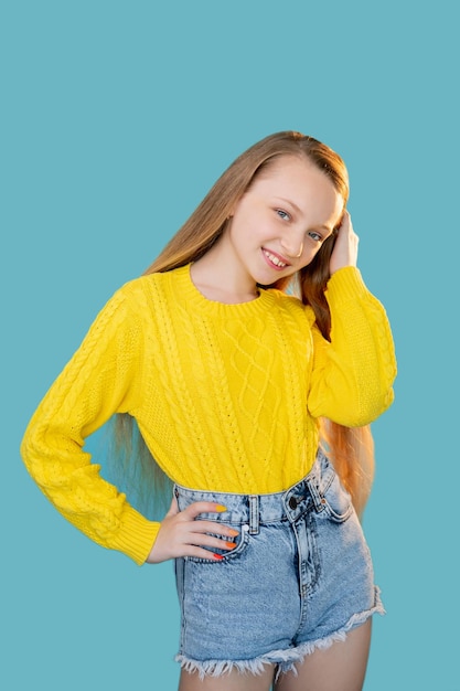 Fröhliches Mädchenporträt Kindermode Lässiger Look Lustige Kindheit Fröhliches junges Modell in gelben Pullover-Denim-Shorts posiert isoliert auf blauem Kopierraumhintergrund