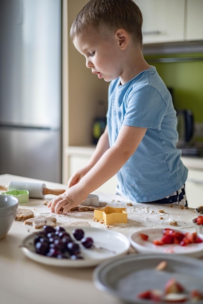 Fröhliches männliches Baby, das hausgemachtes Sommerdessert mit Früchten und Beeren in der Küche zu Hause kocht