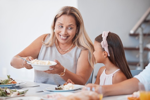 Fröhliches Mittagessen und Großmutter mit Kind am Tisch, das zusammen mit ihrer Familie eine Mahlzeit isst. Glücksgespräch und ältere Frau, die über Essen und Bindung bei einer Dinnerparty oder Veranstaltung zu Hause spricht