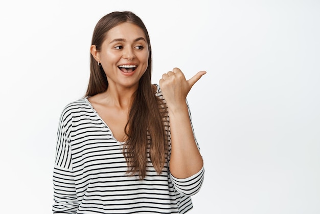 Fröhliches natürliches Mädchen, das lacht, lächelt und mit dem Finger nach rechts auf die Logo-Verkaufswerbung zeigt, neben dem weißen Hintergrund Kopierbereich