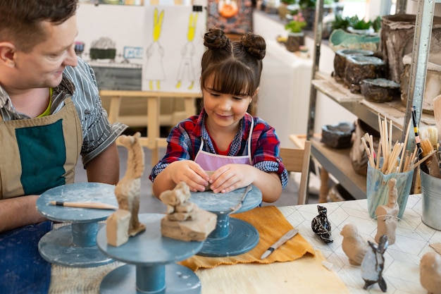 Fröhliches niedliches Schulmädchen, das lächelt, während Ton in der Kunstschule modelliert