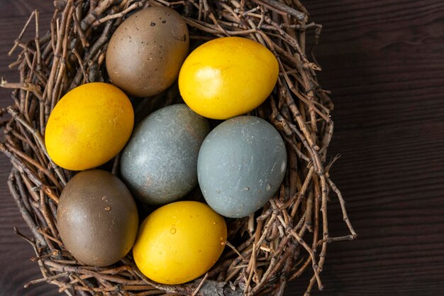 Fröhliches Osterkonzept Mehrfarbige Ostereier im Vogelnest auf Holztisch Draufsicht