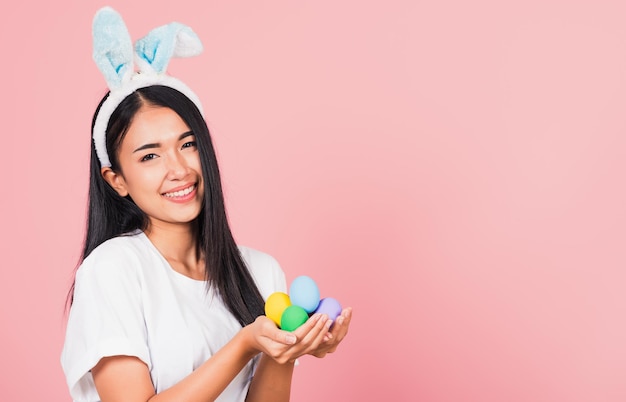 Fröhliches Osterkonzept. Schöne junge Frau lächelnd mit Hasenohren, die ein buntes Osterei-Geschenk auf den Händen halten, Porträtfrau, die in die Kamera schaut, Studioaufnahme isoliert auf rosa Hintergrund