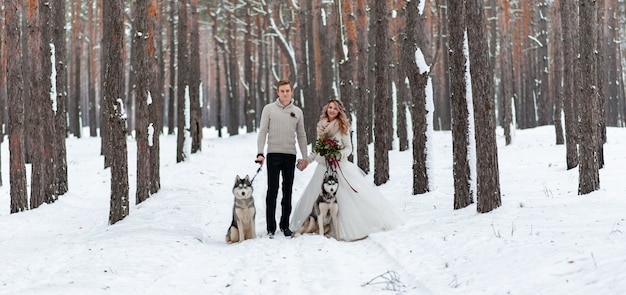 Fröhliches Paar spielt mit Siberian Husky im verschneiten Wald. Winterhochzeit.