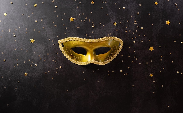 Fröhliches Purim-Karnevalsdekorationskonzept aus goldener Maske und funkelndem Stern auf dunklem Hintergrund. (Frohes Purim auf Hebräisch, jüdische Feiertage feiern)