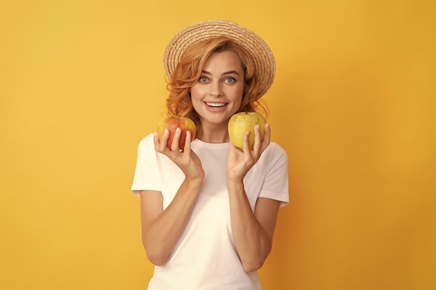 Fröhliches rothaariges Mädchen mit Strohhut hält Apfelvitamin