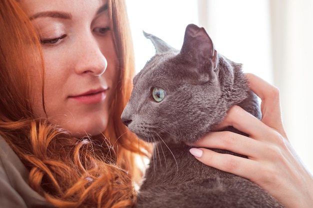 Fröhliches rothaariges Mädchen spielt mit ihrer blauen Katze