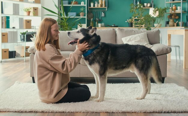 Fröhliches rothaariges Teenager-Mädchen umarmt Streicheleinheiten, ihr Hund spielt Blicke auf das Tier