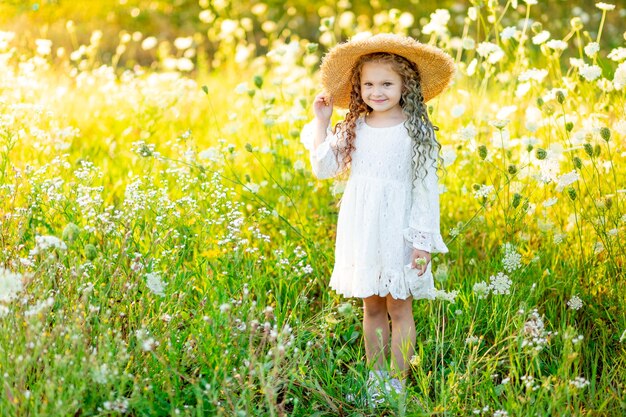 Fröhliches schönes mädchen in einem strohhut im sommer in einem gelben feld mit blumen