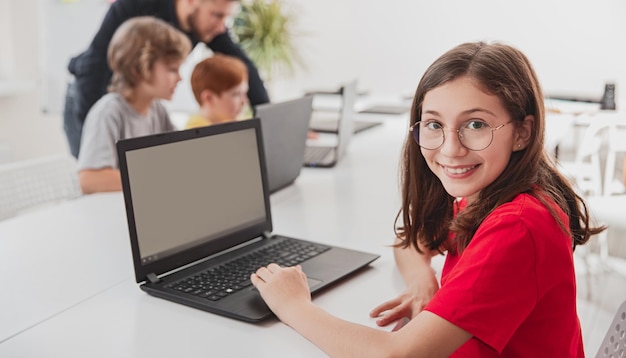 Fröhliches Schulmädchen mit Laptop im Klassenzimmer
