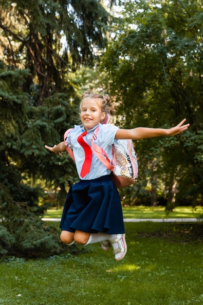 Fröhliches Schulmädchen mit rosa Rucksack springt auf den Hintergrund der Natur.