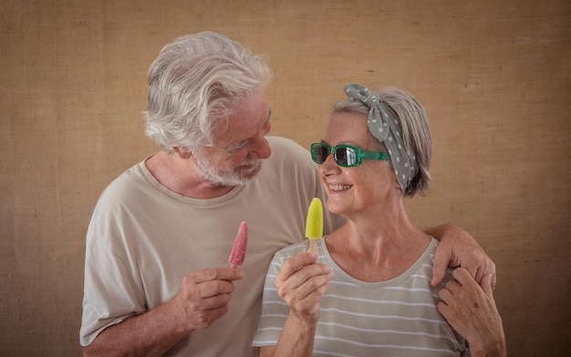 Fröhliches Seniorenpaar, das einen farbigen Eisstiel hält und in die Augen schaut, glückliche Rentner, die den Ruhestand genießen und ein frisches Eis am Stiel essen