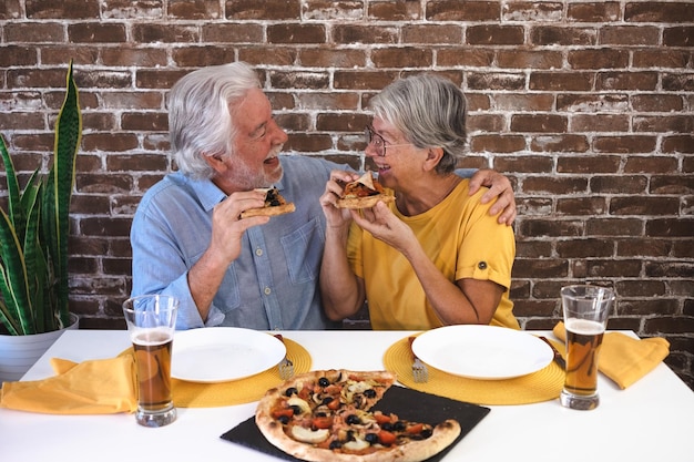 Fröhliches Seniorenpaar, das sich bei Pizza und Bier amüsiert