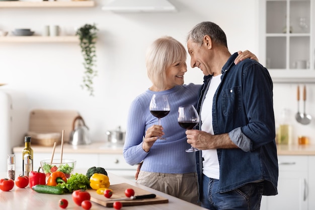 Fröhliches Seniorenpaar klirrt mit Weingläsern in der Küche